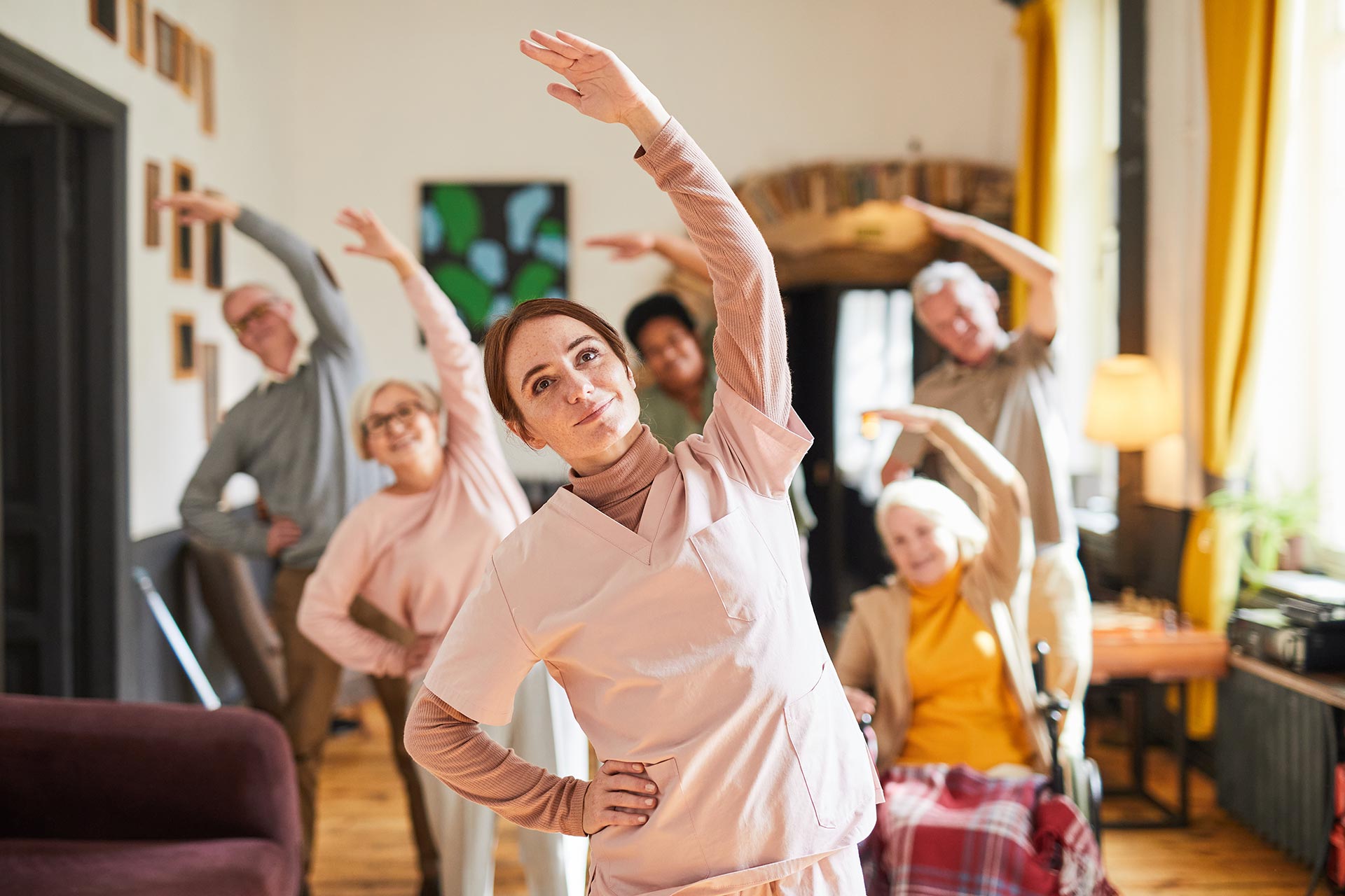 Pflegekraft leitet Gymnastikstunde mit Senior:innen im Pflegeheim